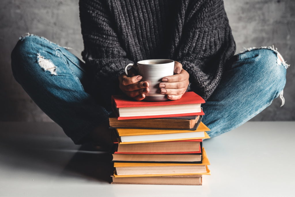 Stack of books with mug on top in front of woman