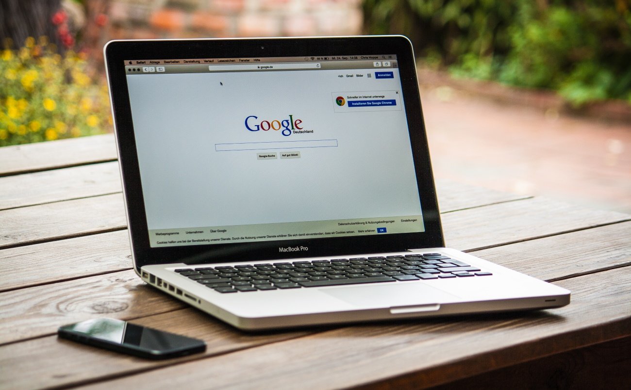 Macbook Pro on wooden table displaying google homepage on screen